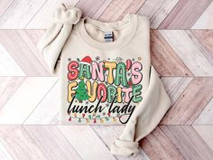 Santa's Favorite Lunch Lady Sweatshirt, Christmas Shirt, Christmas Gift, Christmas Party Shirt, Christmas Gifts For Lunch Lady ❤Reading the Sizing Chart: Please note that the sizing chart includes the measurements of one side of the shirt, not the circumference. ❤Processing Time: 1-3 days ❤How Do I Order 1. Please review all the information provided before placing an order 2. Select the shirt type and size using the drop-down menu. 3.Select the color of the shirt using the following drop-down menu. 4. Proceed with payment ❤ Crafted from supple cotton and adorned with a high-quality print, it becomes an enduring favorite, capturing hearts repeatedly.  Enhanced with ribbed knit collars that lend both style and structure, these t-shirts boast tapered shoulders for an ever-improving fit.  The Thanksgiving Lunch Lady Shirts, Lunch Lady Thanksgiving Shirt, Christmas Lunch Lady Shirt, Bartender Shirts, Football Lover Gifts, Gymnastics Shirts, Gifts For Baseball Lovers, Firefighter Shirts, Chef Shirts