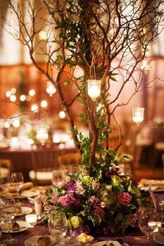 a table set with plates and flowers in front of a candlelight tree decorated with greenery