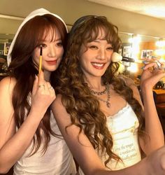 two beautiful young women standing next to each other in front of a mirror holding pencils