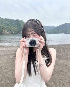 a young woman holding up a camera to take a photo on the beach with mountains in the background