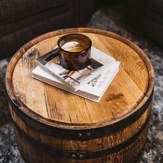 a wooden barrel table with a book on it and a cup of coffee sitting on top