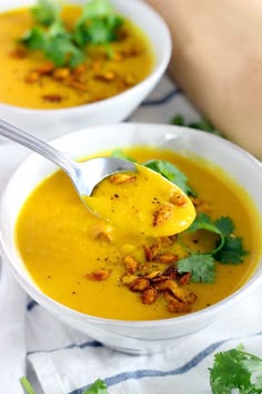 two white bowls filled with soup and garnished with chopped cilantro leaves