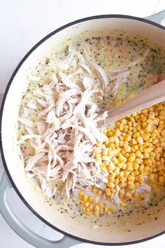 a pot filled with corn and chicken next to a wooden spoon