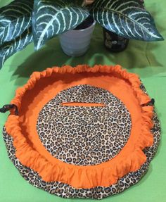 an orange and black animal print pillow sitting on top of a table next to a potted plant