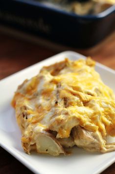 an enchilada on a white plate sitting on a wooden table next to a casserole dish