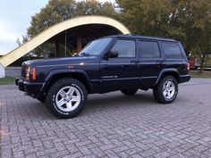 a blue jeep parked in front of a building on a brick road next to trees