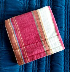 an orange and pink striped blanket laying on top of a blue quilted bed cover