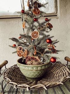 a small christmas tree with oranges and other decorations in a bowl on a wicker tray