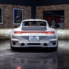 the rear end of a white sports car in a showroom with brick walls and flooring