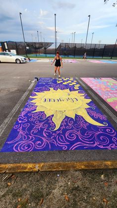 a woman is standing in front of a chalk drawing sun on the ground with purple and yellow colors