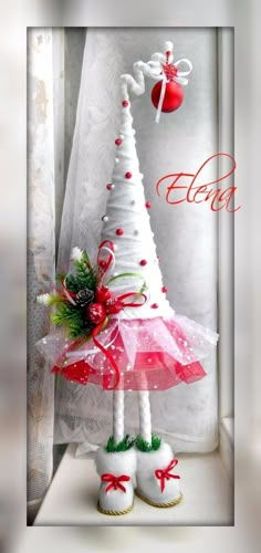 a white christmas tree decorated with red and green decorations, sitting in front of a window