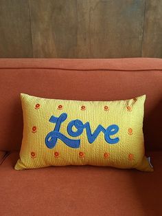 an orange couch with a love pillow on it's back and the word love written in blue