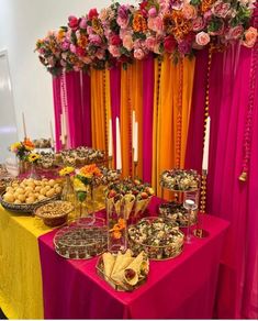 a table topped with lots of food next to colorful drapes covered in flowers and candles