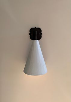 a wall light with a white cone shade hanging from it's side on the wall