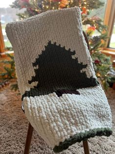 a crocheted blanket sitting on top of a wooden chair in front of a christmas tree