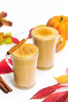 two glasses of pumpkin spice latte on a white surface with autumn leaves and cinnamon sticks