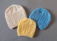 three knitted hats sitting next to each other on top of a gray surface,