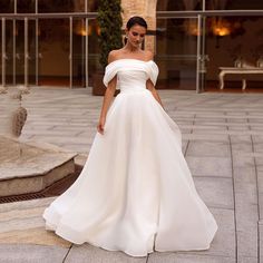 a woman in a white wedding dress is standing outside