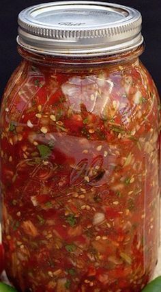 a jar filled with lots of food sitting on top of a table next to an apple