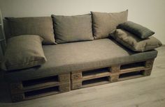 a couch made out of wooden pallets with pillows on top and bottom, sitting in front of a white wall