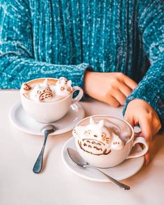 two people sitting at a table with cups of coffee and spoons in front of them