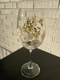 a wine glass with daisies painted on the bottom and yellow flowers in the middle