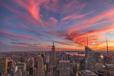 the sun is setting over new york city, with skyscrapers in the foreground