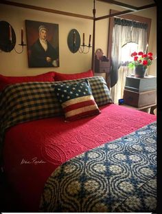 a bed with red and blue comforter in a bedroom next to two paintings on the wall