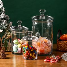 three glass canisters filled with candies next to a christmas tree on a table