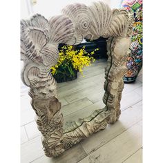 a decorative mirror sitting on top of a wooden floor next to a vase with yellow flowers