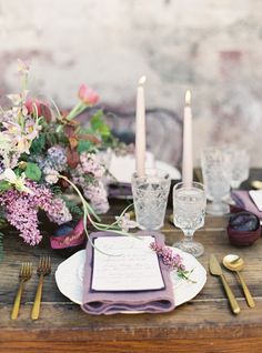 the table is set with purple and white plates, silverware, candles, and flowers