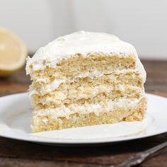 a piece of cake with white frosting on a plate next to a lemon slice