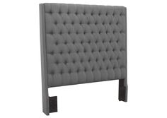 an upholstered headboard with black legs and buttons on the top, in grey fabric