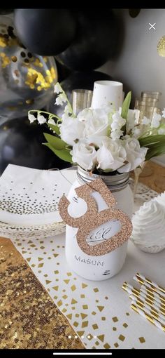 a table topped with a vase filled with white and gold flowers next to a black balloon