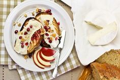 a plate with bread, fruit and cheese on it next to some slices of bread