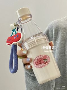 a woman holding a glass bottle with an animal keychain attached to it's side