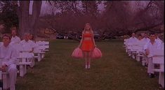 a woman in a short red dress walking down the aisle at an outdoor wedding ceremony