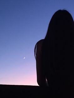 the silhouette of a woman sitting in front of a sunset with a half moon behind her