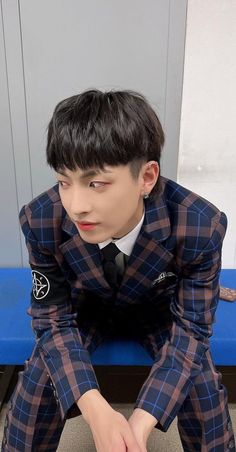 a young man sitting on top of a blue bench wearing a plaid suit and tie