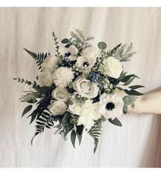 a bouquet of white flowers and greenery is held by a woman's hand