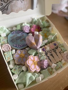 a box filled with assorted decorated cookies on top of a wooden table next to a window