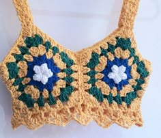 a crocheted bra hanging from a hook on a white wall with blue and green flowers