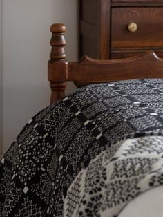 a bed with a black and white blanket on top of it next to a wooden dresser