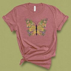 This unique butterfly floral Shirt, has a vintage botanical feel to it, with an intricate flower design. This cute boho shirt, makes a great gift for mom, for mothers day, gift for her or gift for the garden lover. This shirt is great for a warm spring or summer day, a festival, brunch or afternoon in the garden. DETAILS This Beautiful graphic t-shirt is made of 49% to 100% combed and ring-spun cotton and is very soft and comfortable to wear. Check the size card for specific fabrications per col Casual T-shirt With Floral Embroidery For Gift, Bohemian Spring T-shirt With Vintage Print, Spring Bohemian T-shirt With Vintage Print, Bohemian Vintage Print T-shirt For Spring, Pink Bohemian T-shirt For Spring, Casual Floral Print Top Gift, Bohemian Cotton Tops With Butterfly Print, Floral Print Summer Tops As A Gift, Casual Floral Print Tops As Gift