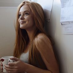 a woman with long red hair holding a coffee cup and looking up at the sky