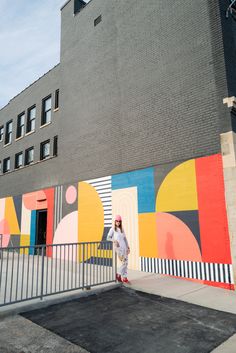 a person standing in front of a building with a colorful mural on it's side