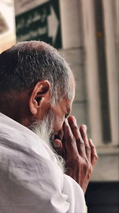 an old man with white hair and beard is holding his hands to his face as he looks off into the distance