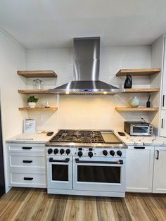 a stove top oven sitting inside of a kitchen next to wooden flooring and open shelving