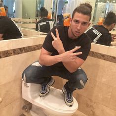 a man sitting on top of a white toilet in a bathroom next to a sink