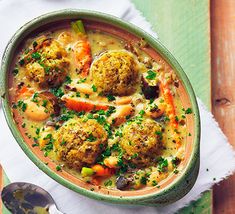 a bowl filled with meatballs and vegetables on top of a white cloth next to a spoon